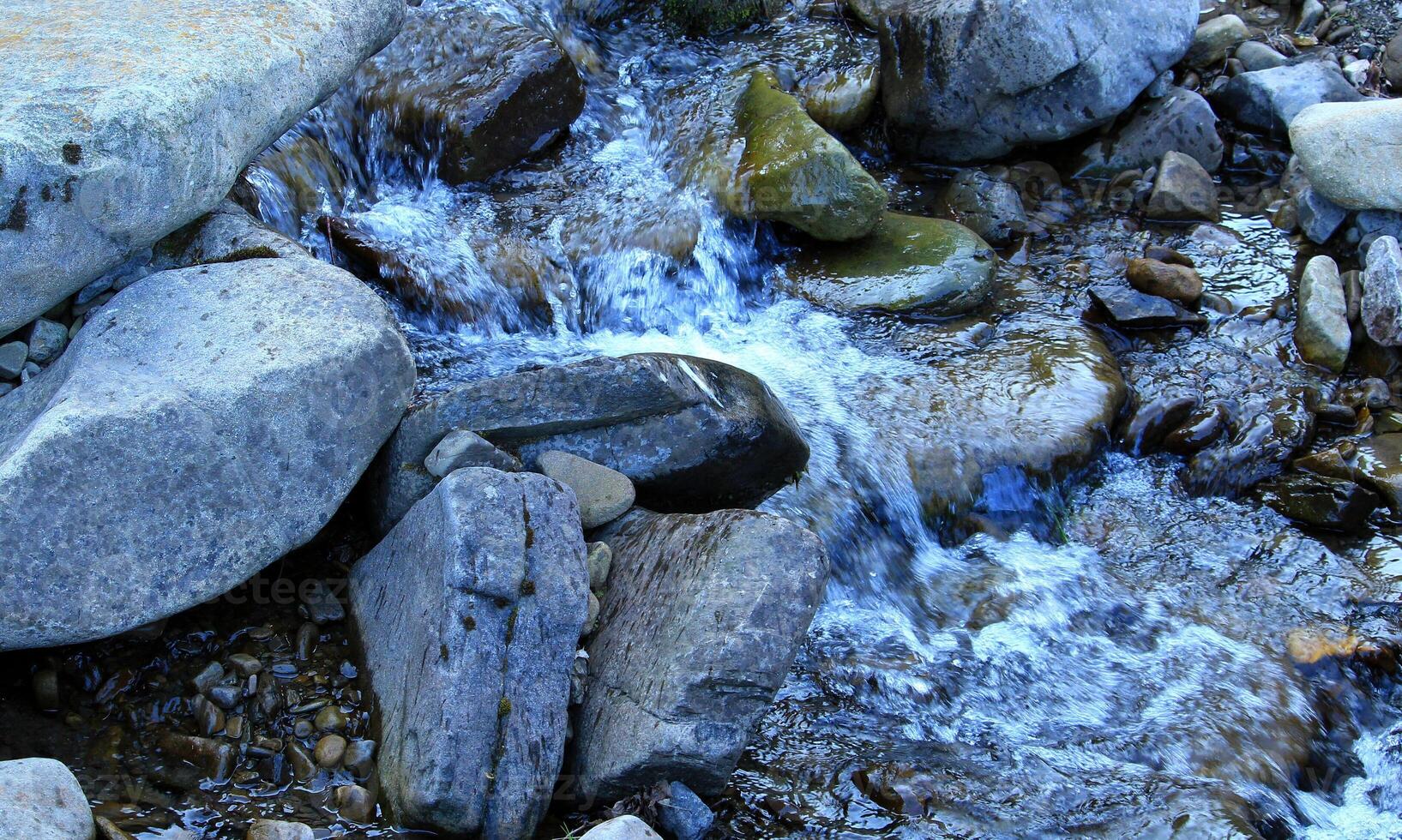A stream of water flows in a stream, bending around boulders and stones photo