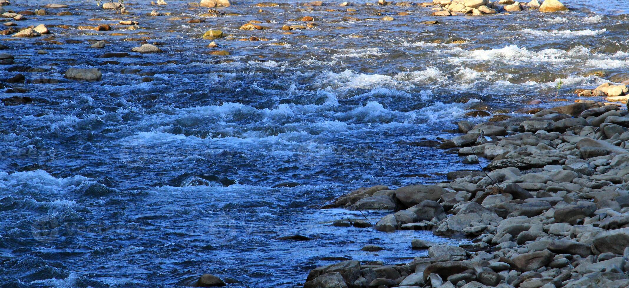 A stream of water flows in a stream, bending around boulders and stones photo