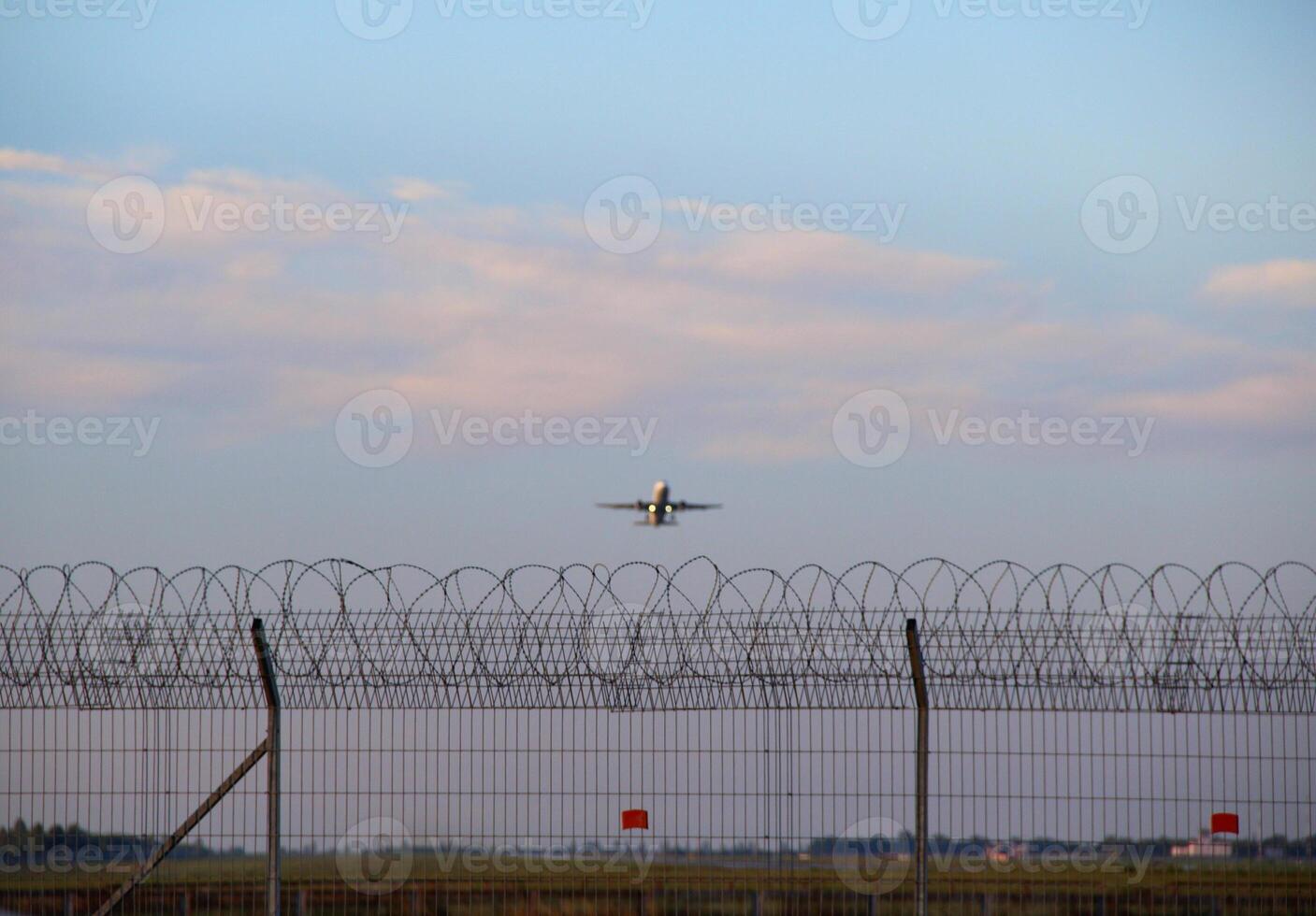 A Passenger Plane Is Taking Off Over A Fenced Airport Runway photo