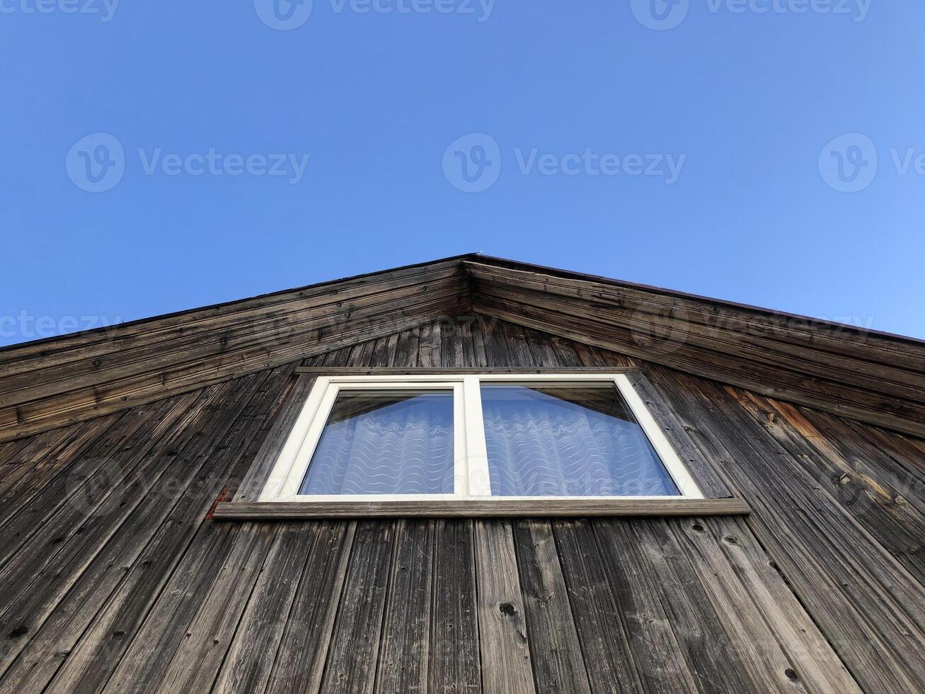 white window on the gable of a rustic wooden house, blue sky, low angle view photo