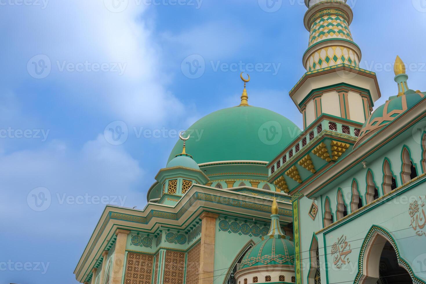 Beautiful close-up symmetry of the mosque with dominant colors of green and gold and a blue sky background photo
