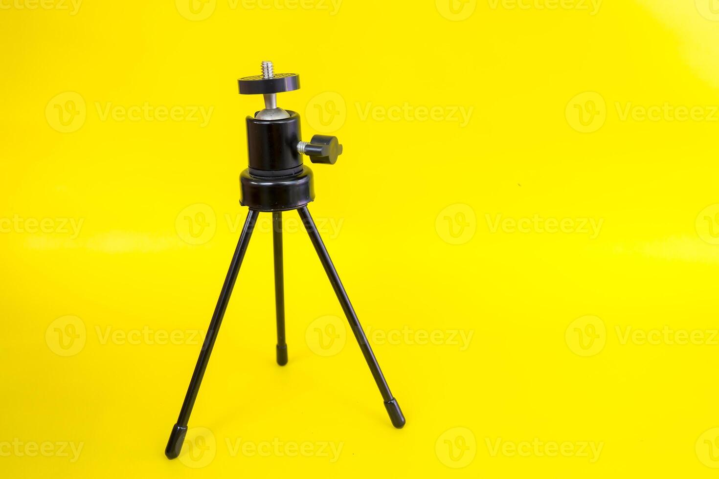 Black mini tripod with steel case and ballhead isolated on yellow background photo