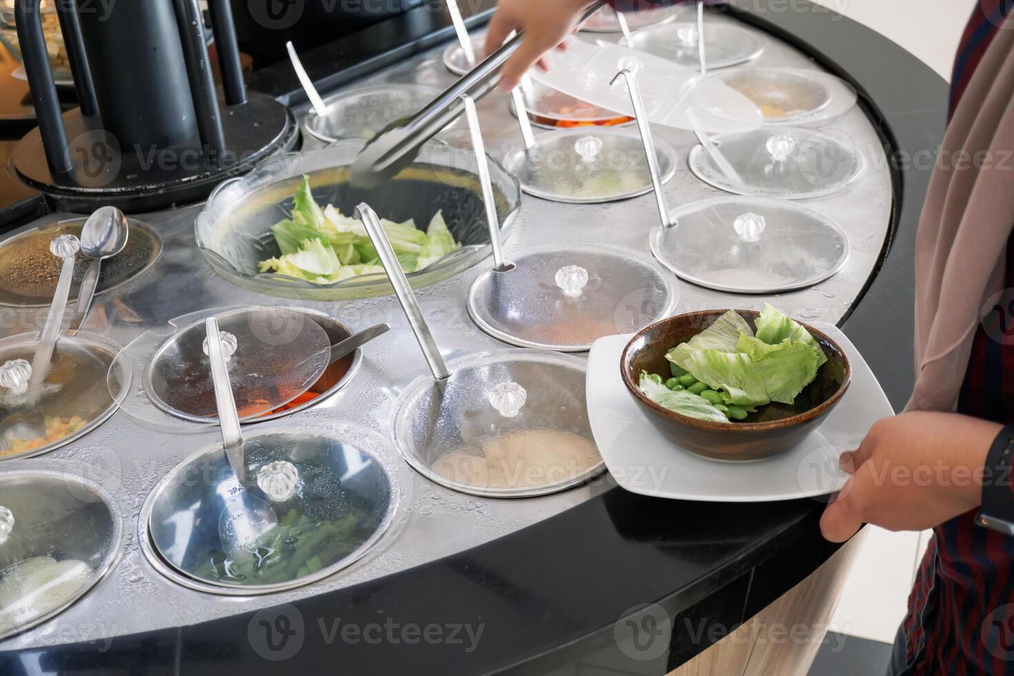 Fresh Salad bar counter with someone's hands lifting vegetables into a bowl. photo