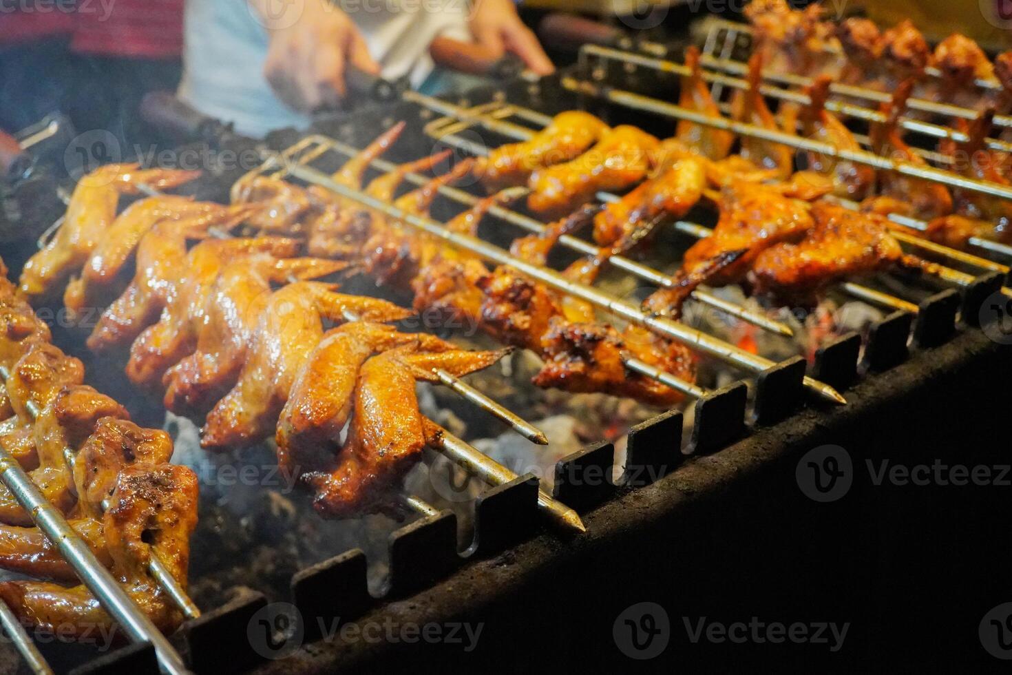 Grilling chicken wings with charcoal that is turned manually by hand photo