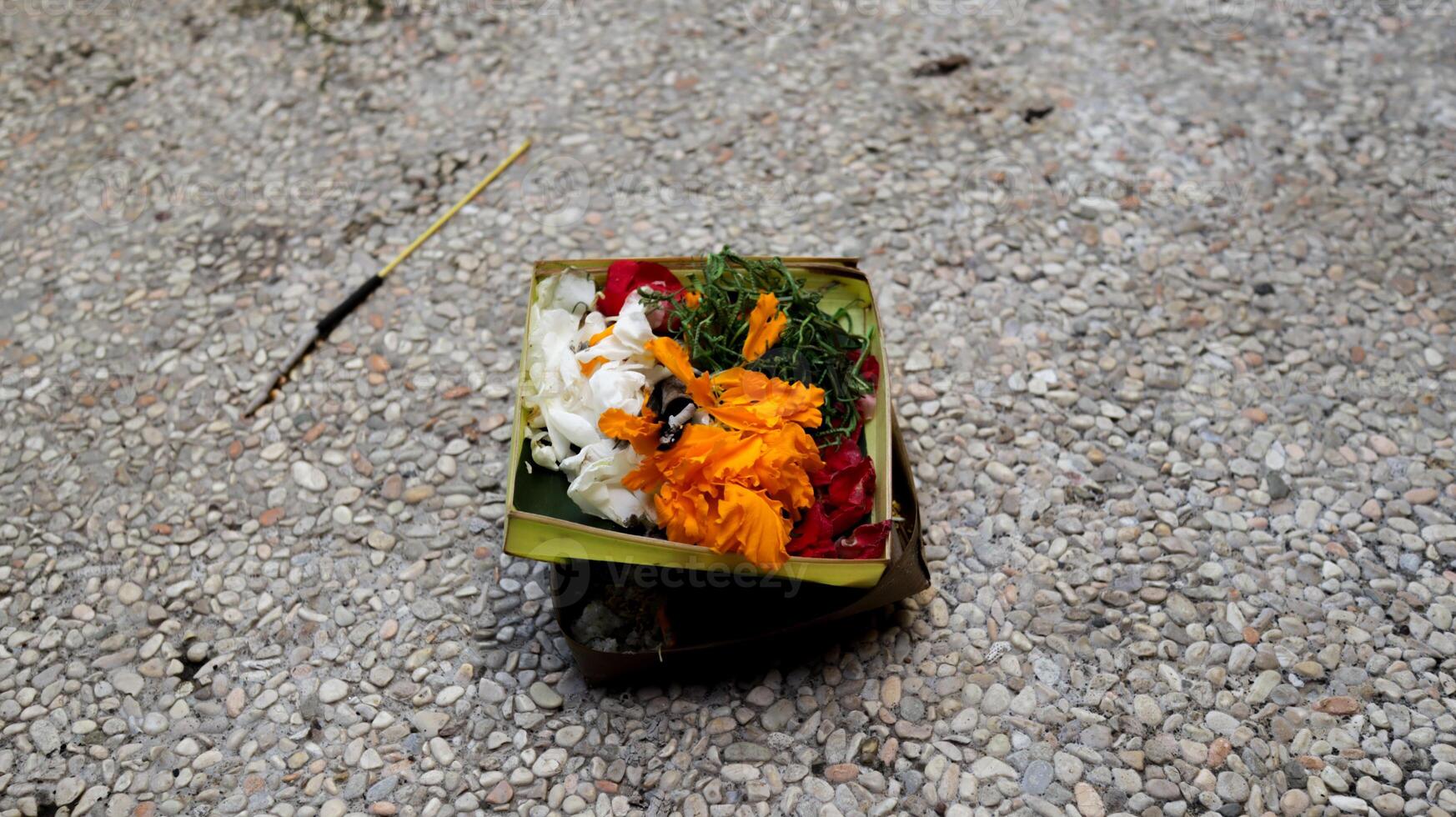 Beautifully Arranged Balinese Offering Basket with Colorful Flowers on Pebbled Ground for Traditional Hindu Rituals in Bali. photo