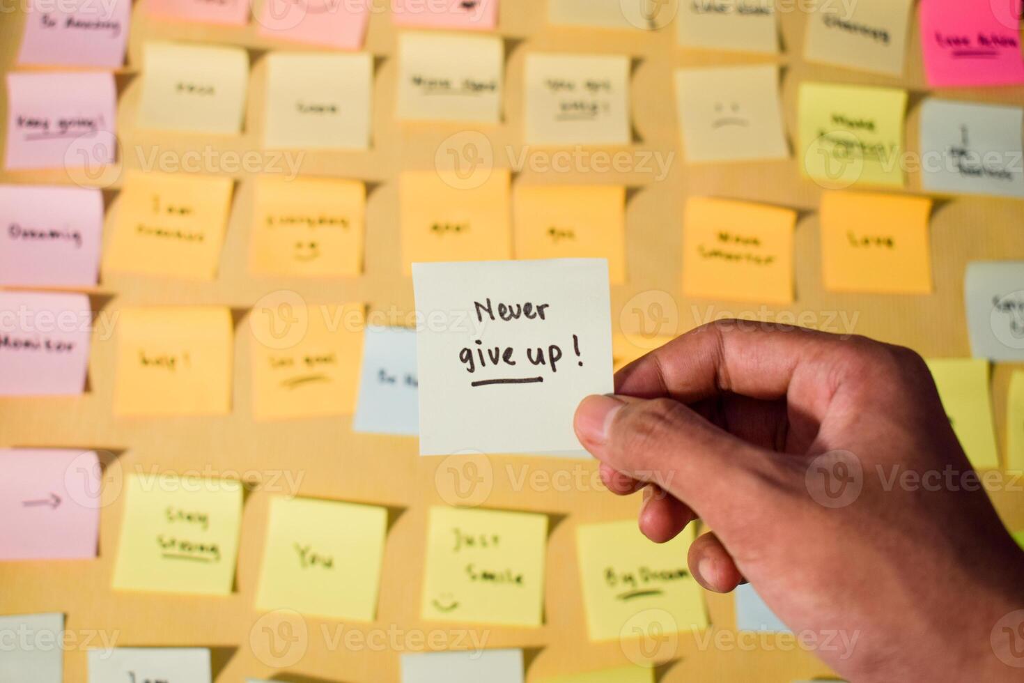 Hand hold sticky notes with words Never Give Up. Motivational words for personal development, inspirational handwriting. Sticky notes background photo