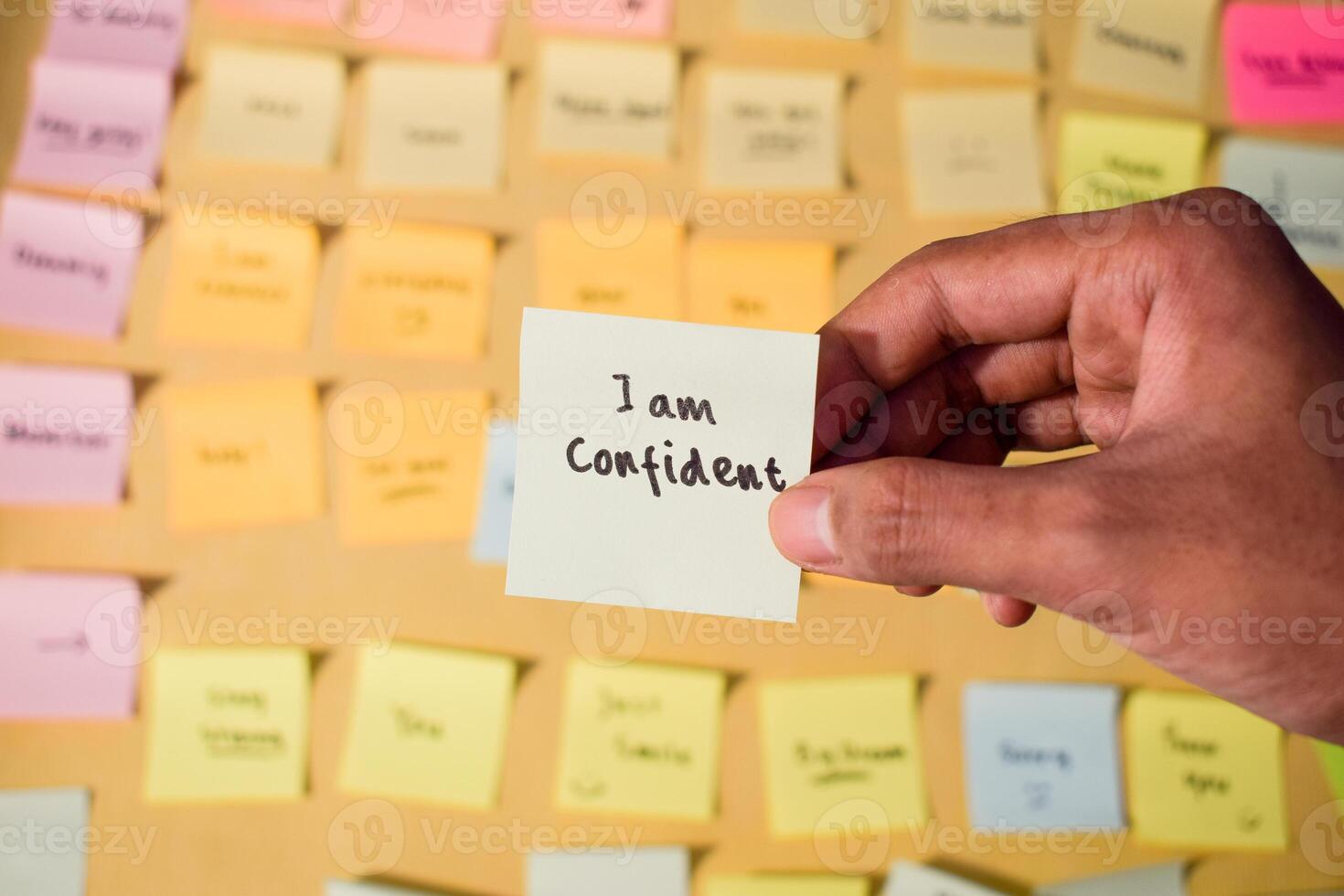 Hand hold sticky notes with words I am confident. Motivational words for personal development, inspirational handwriting. Sticky notes background photo
