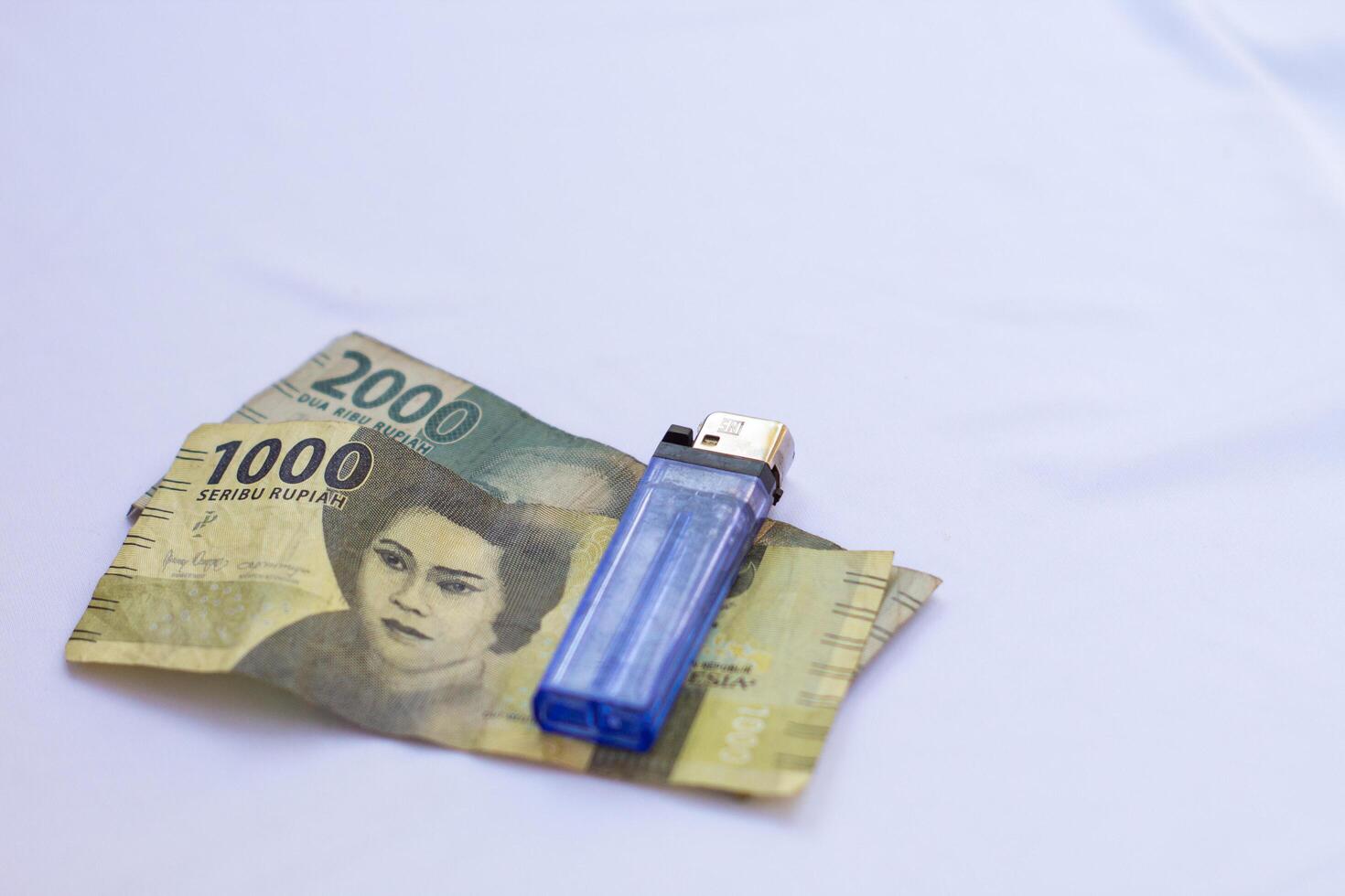 indonesia 4 september 2024, 2000 rupiah banknotes 1000 rupiah banknotes and a blue lighter photographed close up from a side angle with an isolated background photo