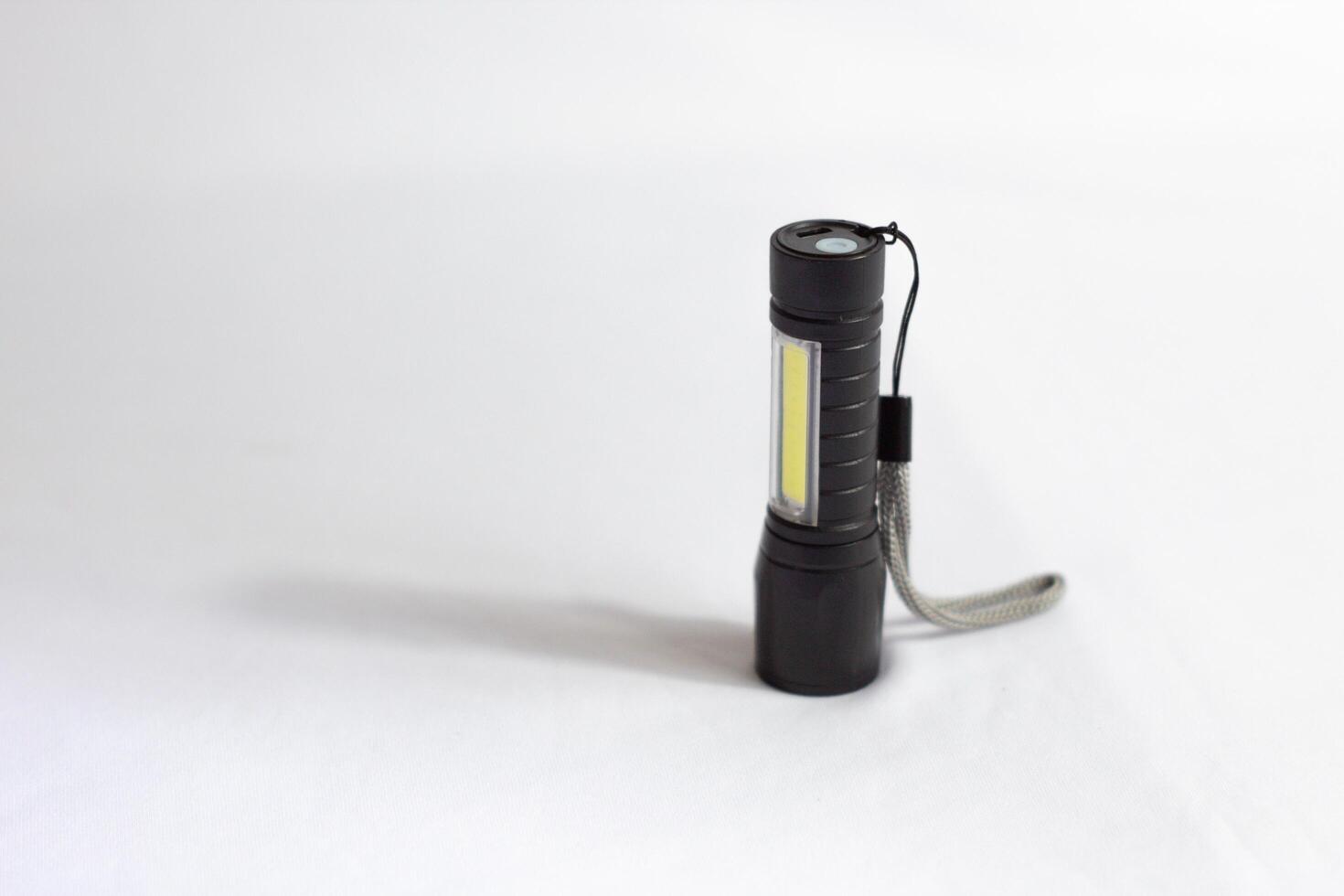 Modern black metal LED flashlight. Portable flashlight with white background. photo