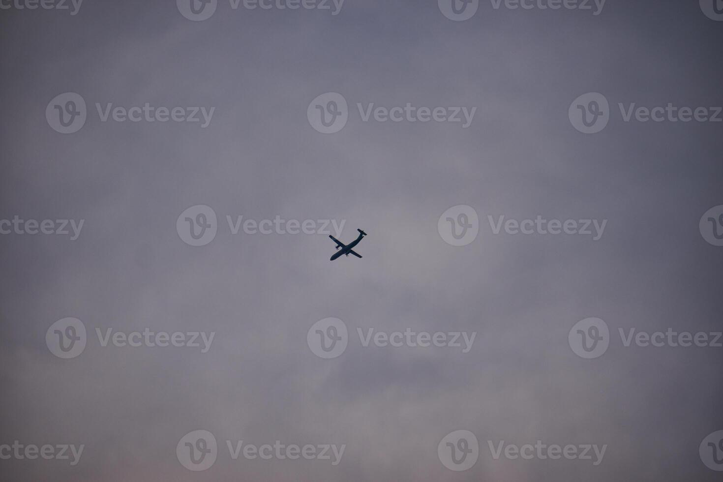 Silhouette of an airplane flying in the middle of a white cloudy sky photo