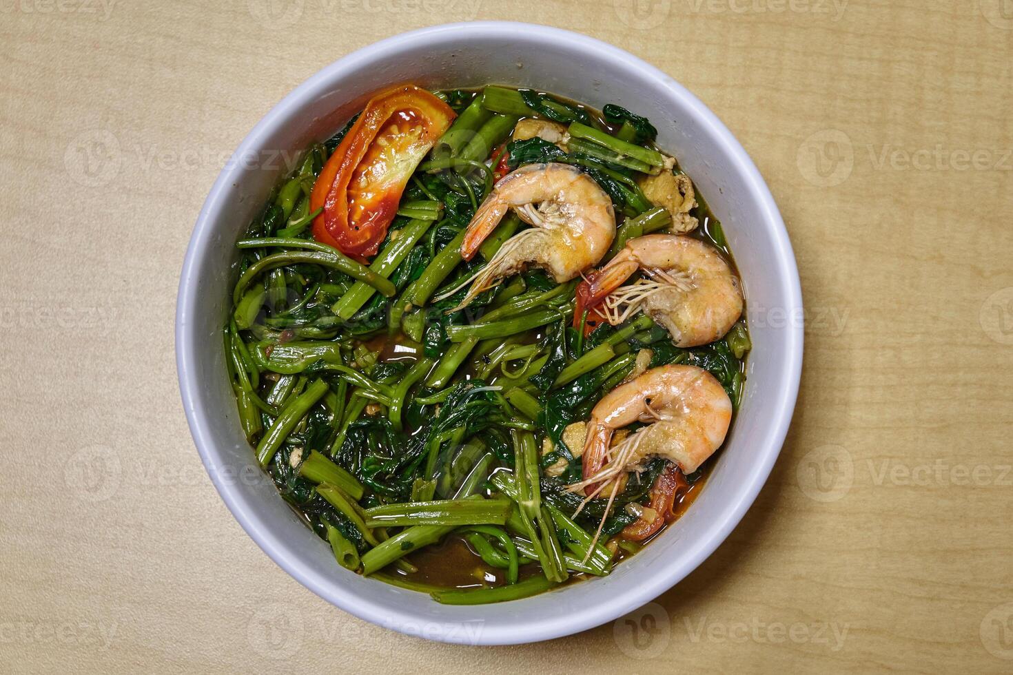 Top view of stir-fry water spinach or kangkong with shrimps on white bowl on wooden background photo