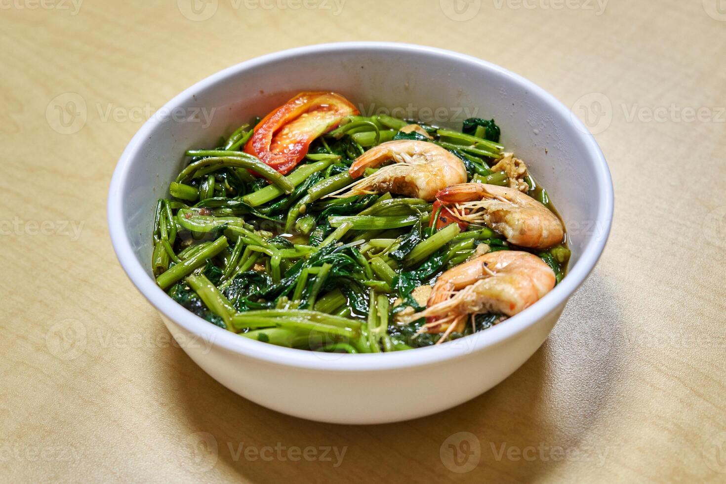 Stir-fry of kangkong or water spinach with shrimps isolated on white bowl on wooden background photo
