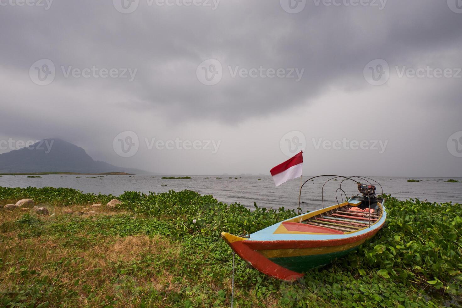 A wooden boat moored on the edge of a lake under cloudy sky photo