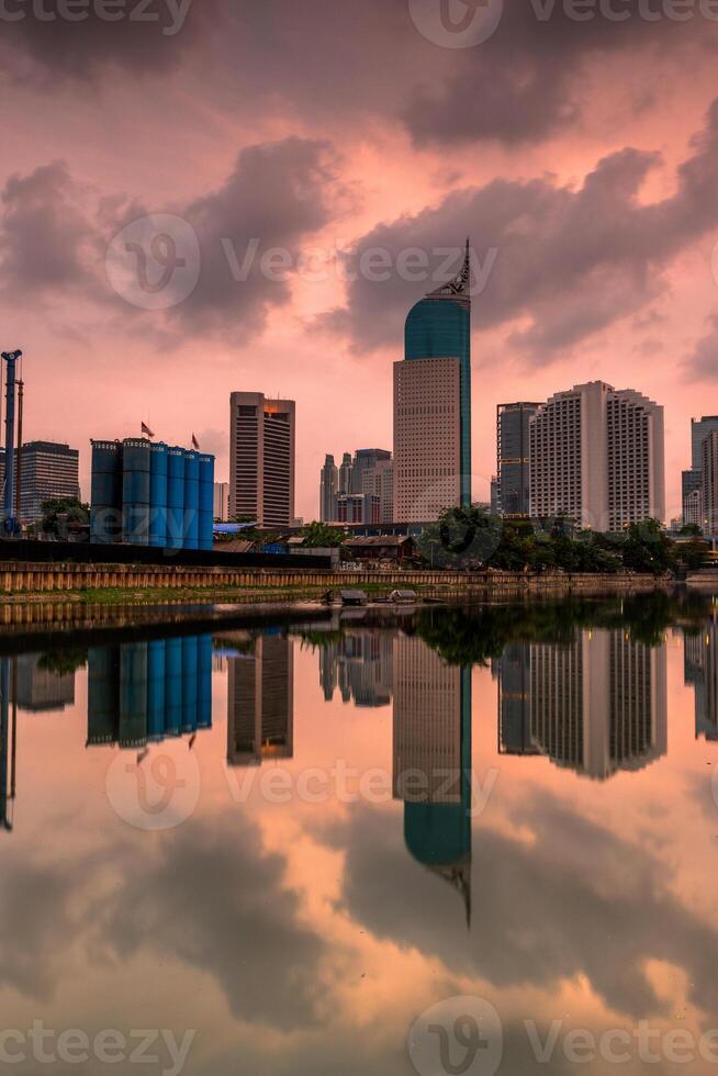 Jakarta skyline under cloudy sky. Office buildings tower of Jakarta city reflected on water with clouds on sky photo
