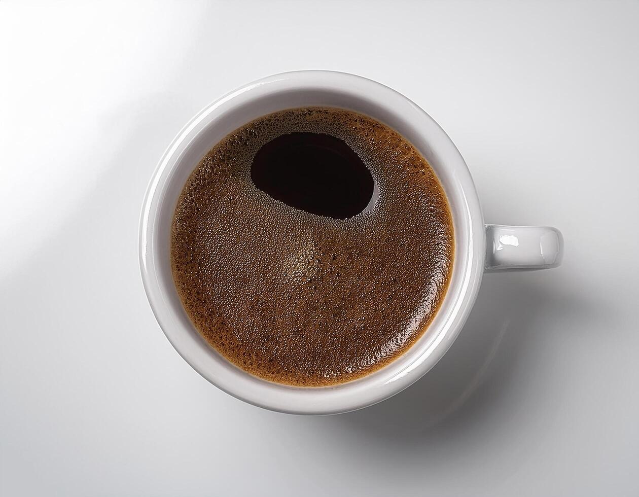 A cup of black coffee with froth on top, placed on a white surface photo