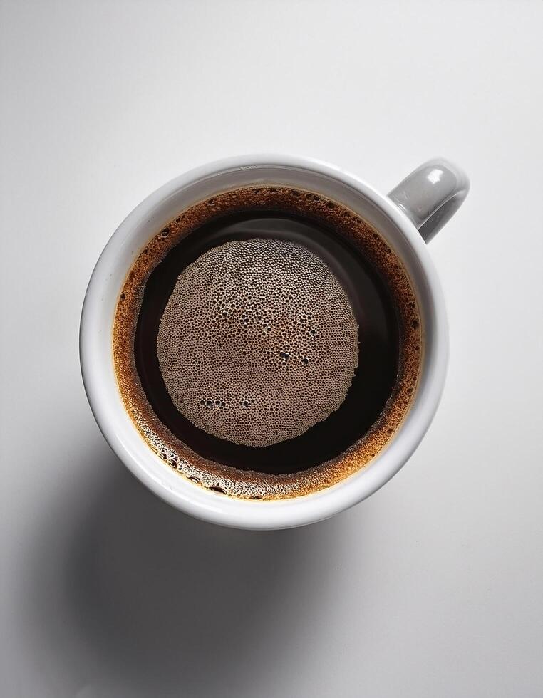 A cup of black coffee with froth on top, placed on a white surface photo