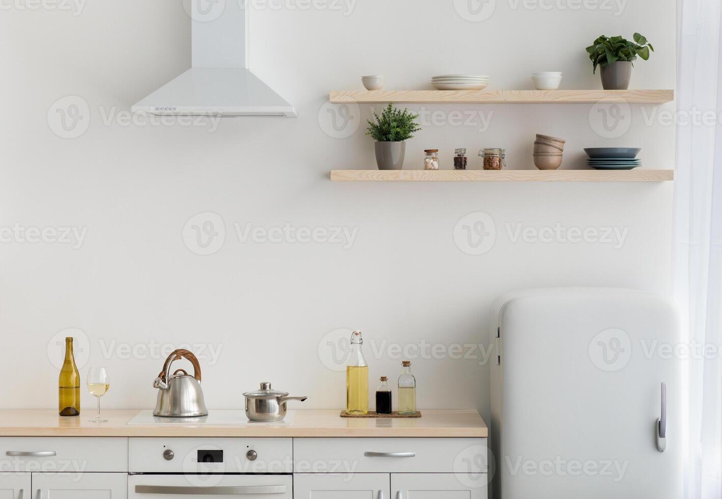 Modern minimalist white kitchen in scandinavian style, simple, minimalist interior. Refrigerator, shelves with crockery and plants in pots, furniture and stove with utensils, light wall, free space photo