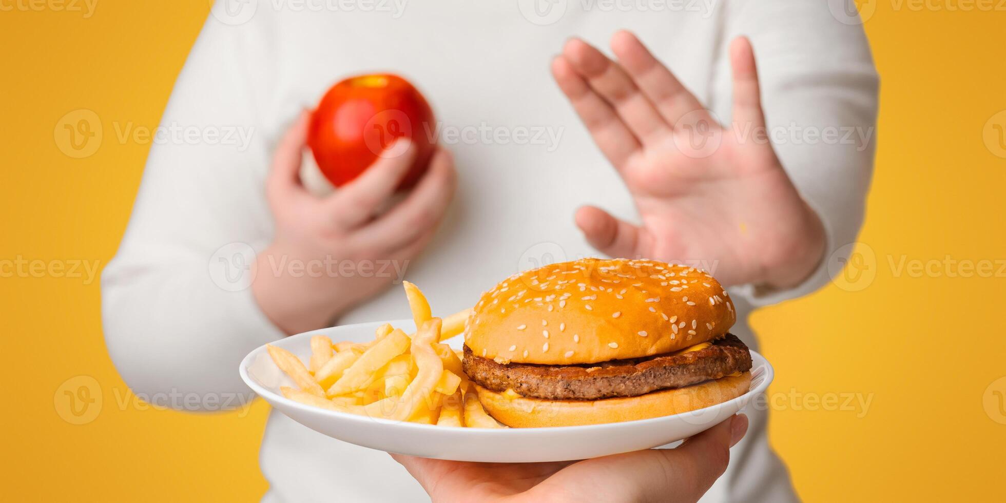 Unrecognizable plus size girl refusing to eat fast junk food, showing stop gesture with hand and choosing apple photo