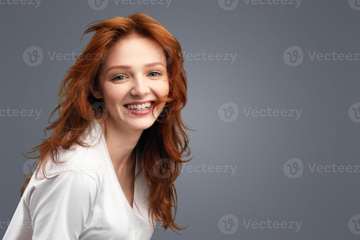Beauty Portrait Of Cute Red-Haired Young Lady Smiling To Camera Standing Over White Background, Wearing T-Shirt. Cheerful Teen Posing In Studio. Youth, Positive Emotions Concept photo