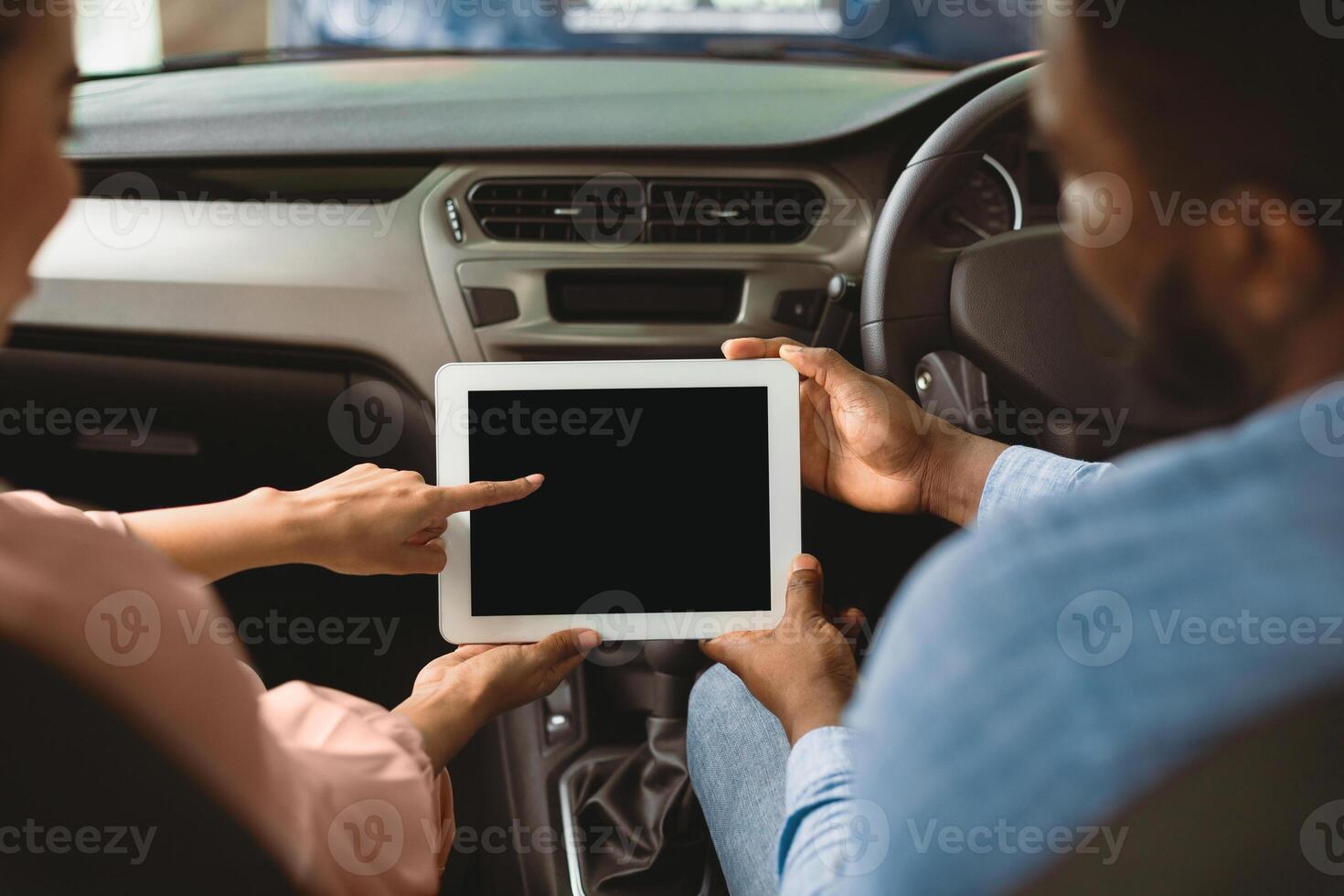 Afro Couple Using Digital Tablet With Empty Screen Sitting In New Car In Dealership Center. Mockup, Back View, Selective Focus photo