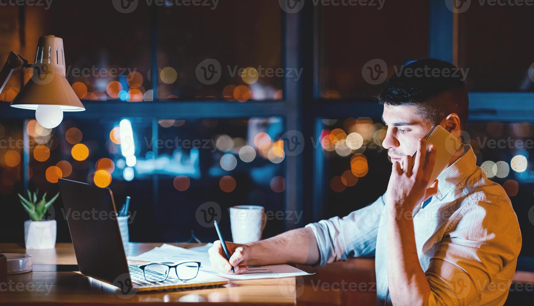Overnight Work. Tired Manager Guy Calling On Phone Taking Notes Working In Office At Night. Empty Space photo