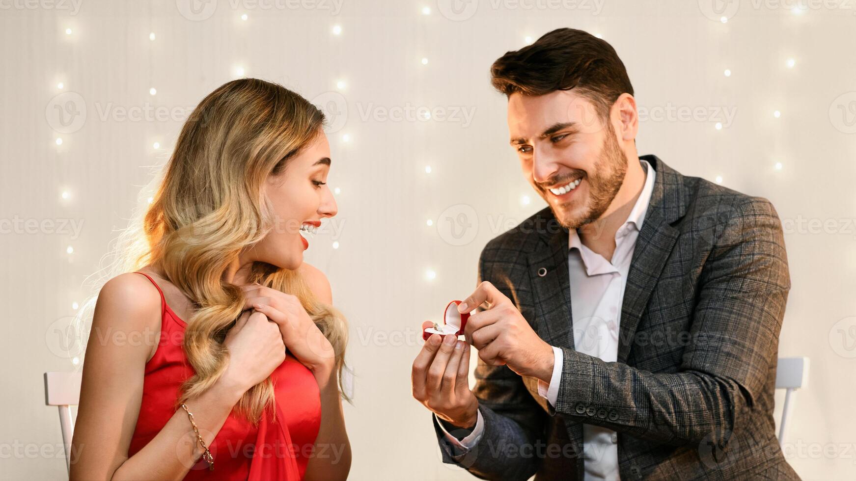 Loving man making proposal to his surprised girlfriend on romantic date in restaurant, presenting engagement ring photo