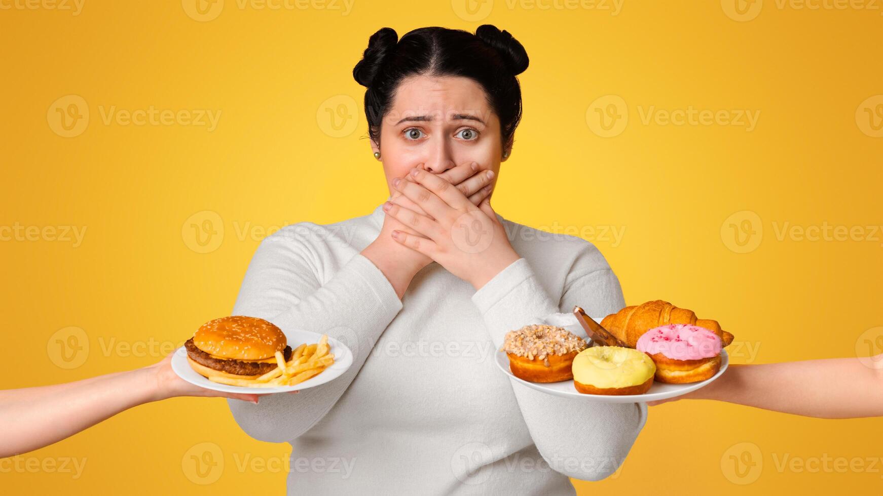 Overeating Concept. Concerned Plus Size Girl Covering Mouth With Hands, Rejecting To Eat Offered Junk Food, Standing On Yellow Background, Copy Space photo