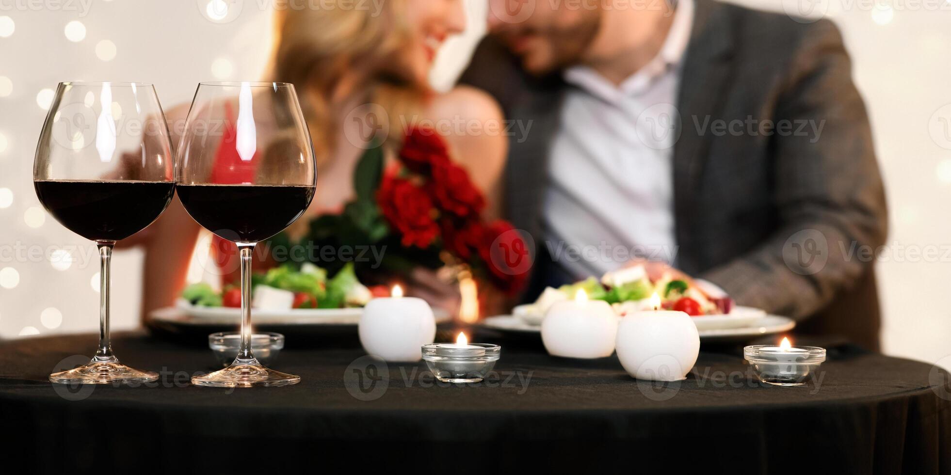 Valentine's Day Dinner Concept. Two Glasses With Red Wine On Table, Romantic Couple Blurred In Background photo