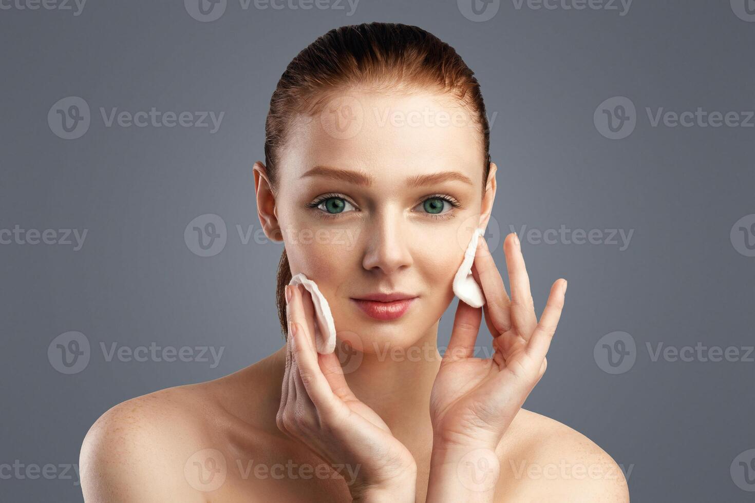 Ginger-Haired Girl Cleansing Skin With Cotton Pads Looking At Camera Posing Caring For Face Over White Studio Background. Facial Skincare And Cosmetics, Clean Skin Concept. Beauty Portrait photo