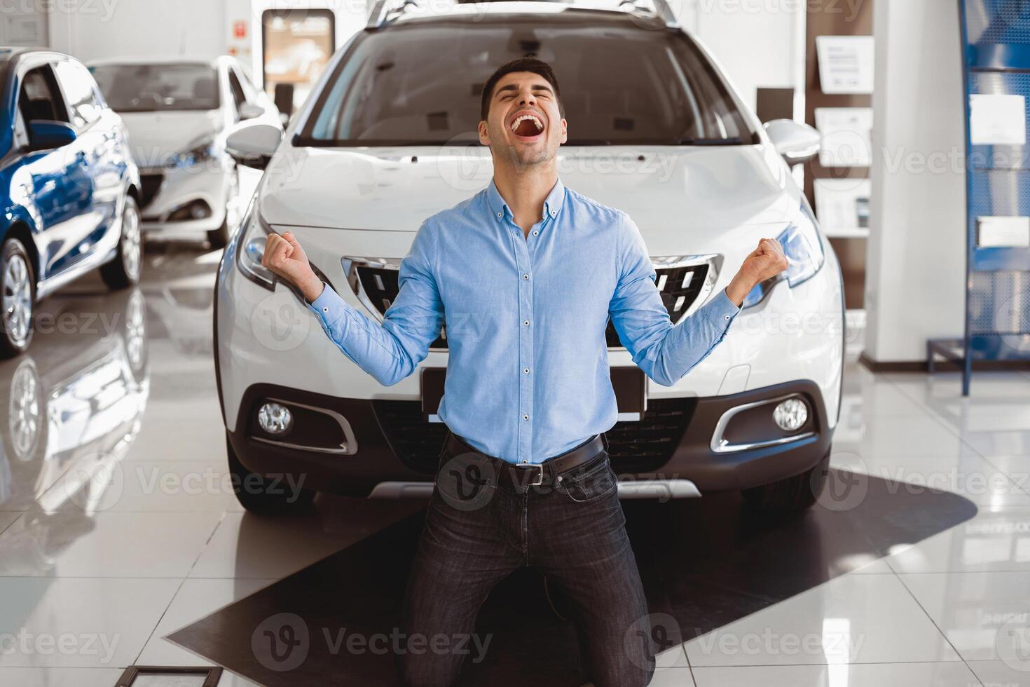 Yes, That's My New Car. Elated excited man kneeling in front of his auto in dealership office, making winner gesture photo