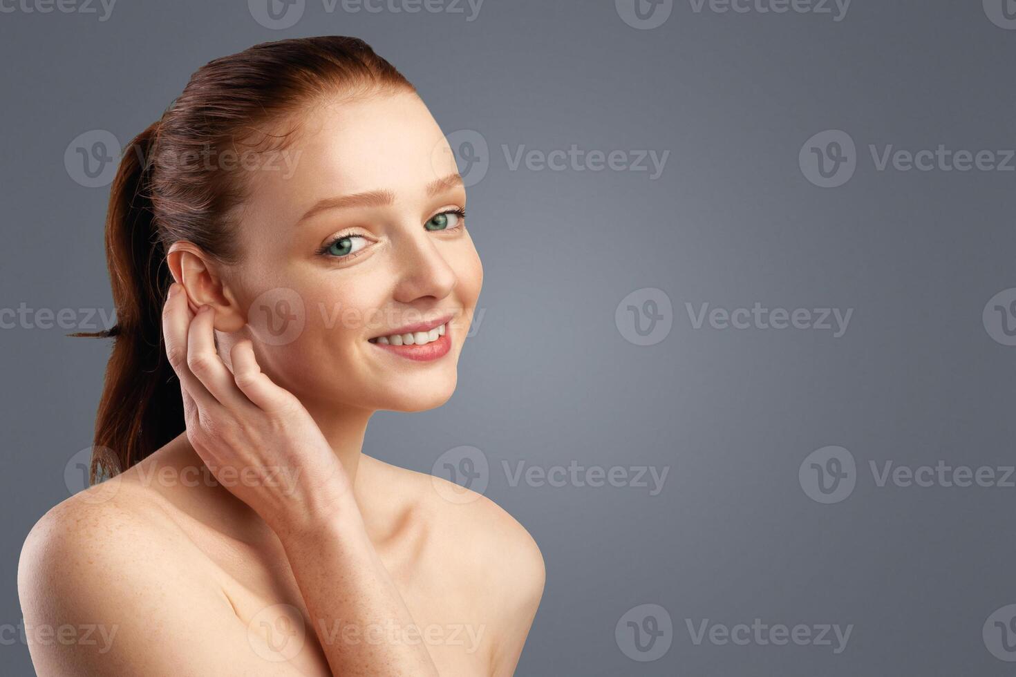 Haircare. Ginger-Haired Young Woman With Ponytail Hairstyle Posing Touching Smooth Red Hair Standing In Studio Over White Background, Smiling To Camera. Youth, Female Beauty Portrait Concept photo