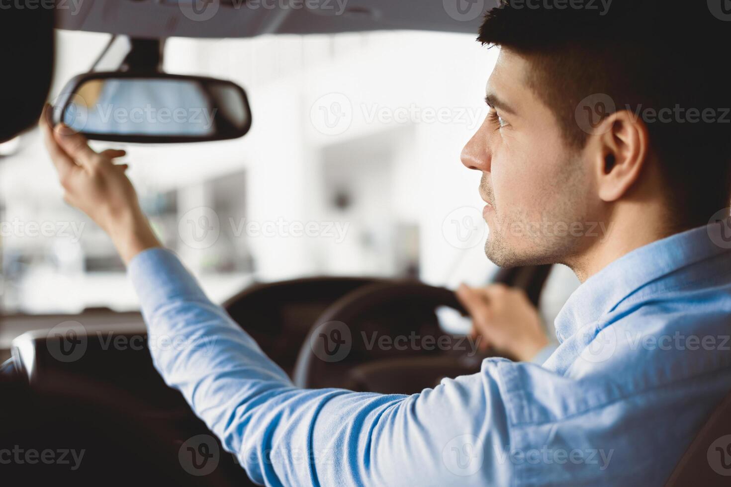 Young Man Touching And Looking At Rearview Mirror Sitting In Driver's Seat Testing New Auto photo