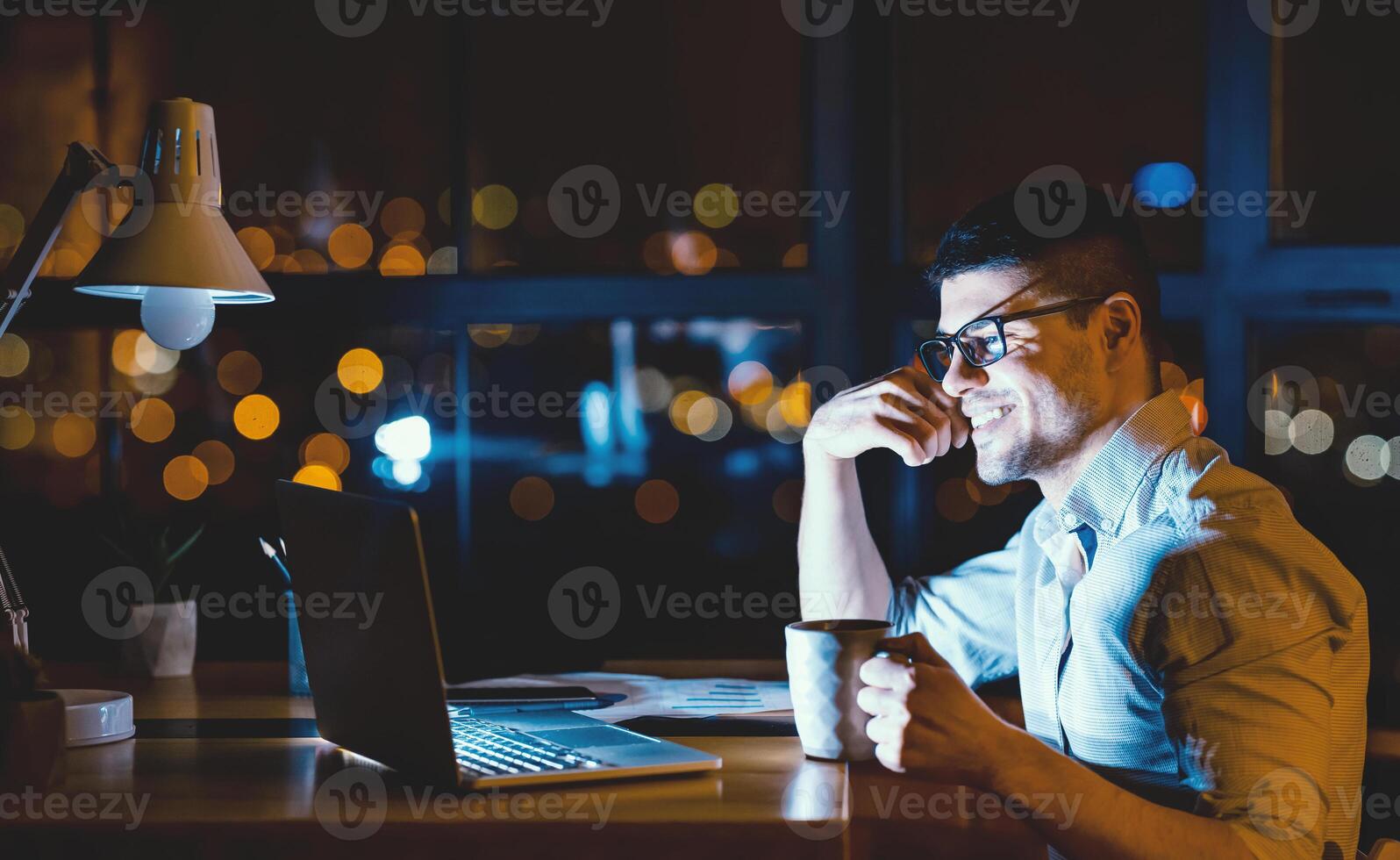 Business Guy Sitting At Laptop Having Coffee In Modern Office At Night. Corporate Lifestyle. Copy Space photo