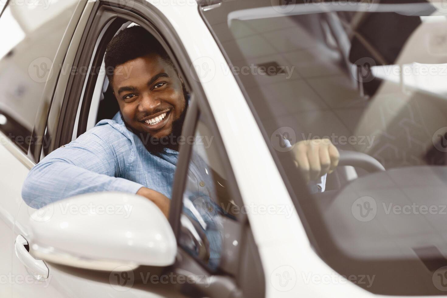 Car Owner. Joyful Afro Guy Smiling To Camera Sitting In New Automobile Driving From Dealership Shop. Selective Focus photo