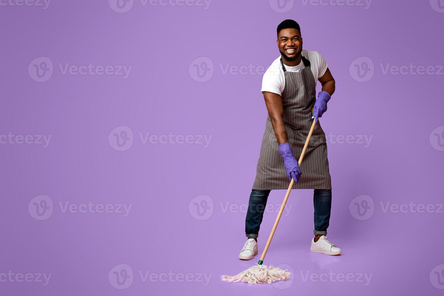 Household Chores. Happy African Janitor Washing Floor With Mop And Smiling To Camera While Posing Over Pink Background In Studio photo