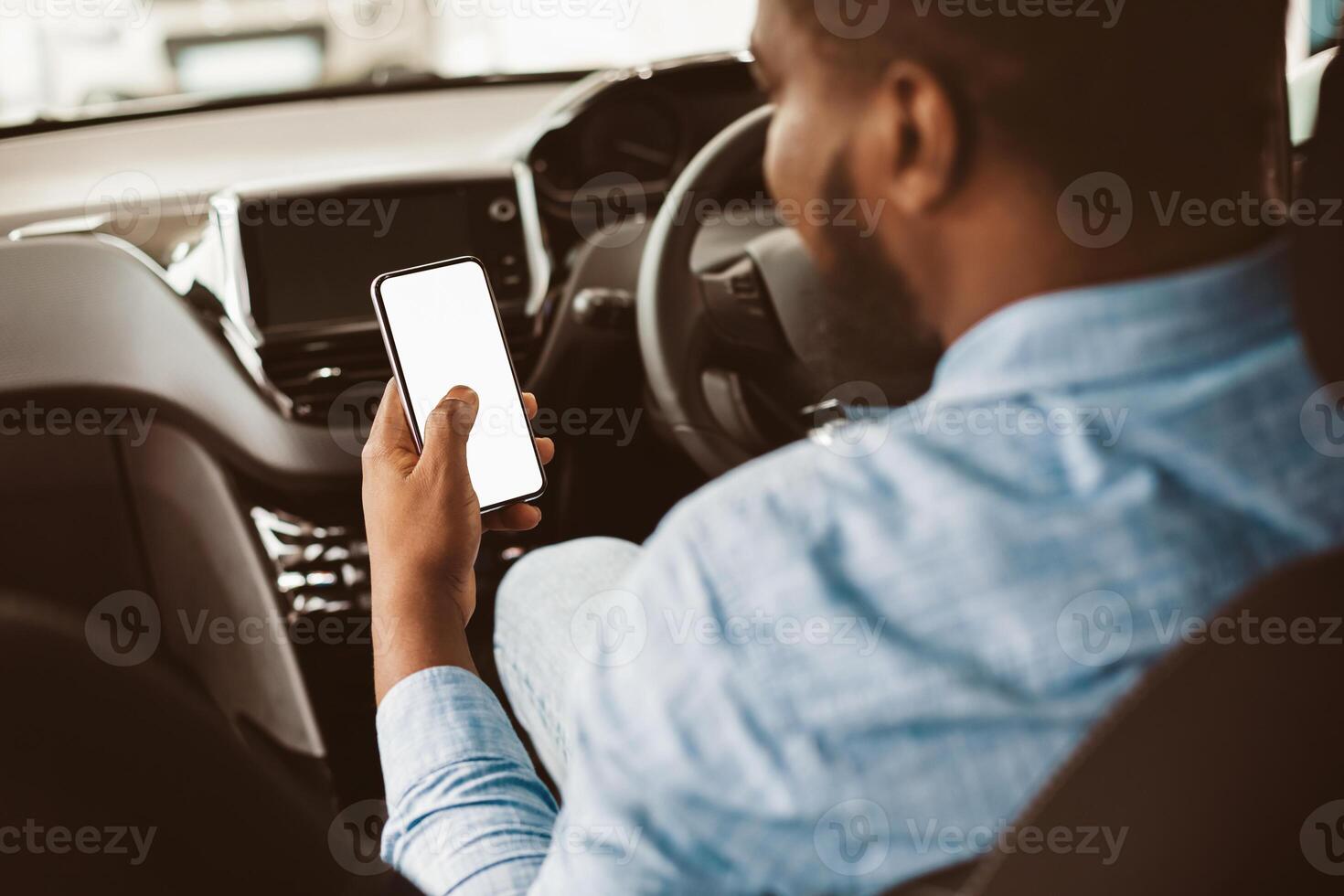 Car Driving App. African American Man Using Phone With Empty Screen Sitting In Auto Vehicle. Selective Focus, Mockup, Back View photo