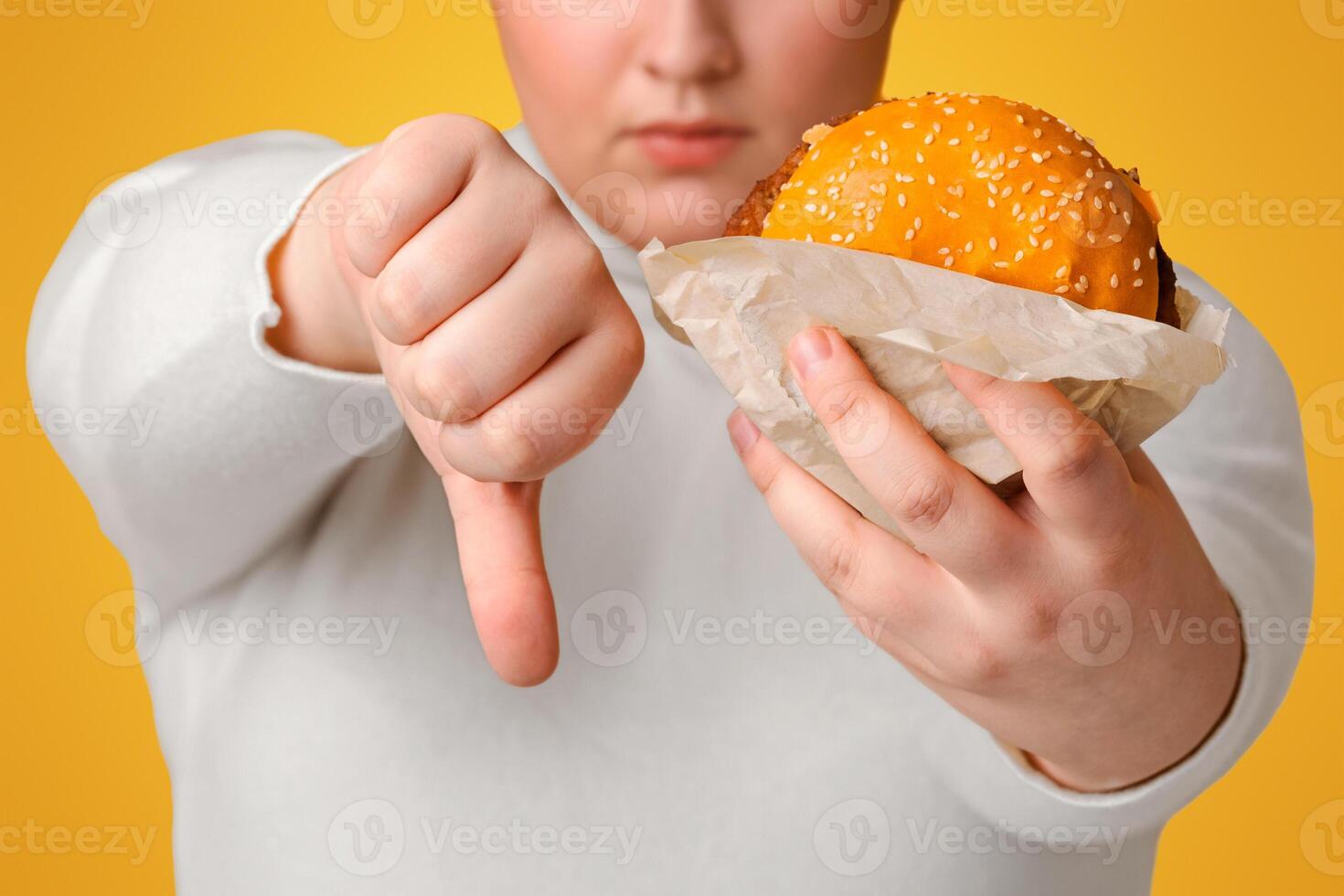 Artificial Flavors In Fast Food Concept. Unrecognizable Overweight Woman Holding Burger And Showing Thumb Down Gesture, Cropped photo