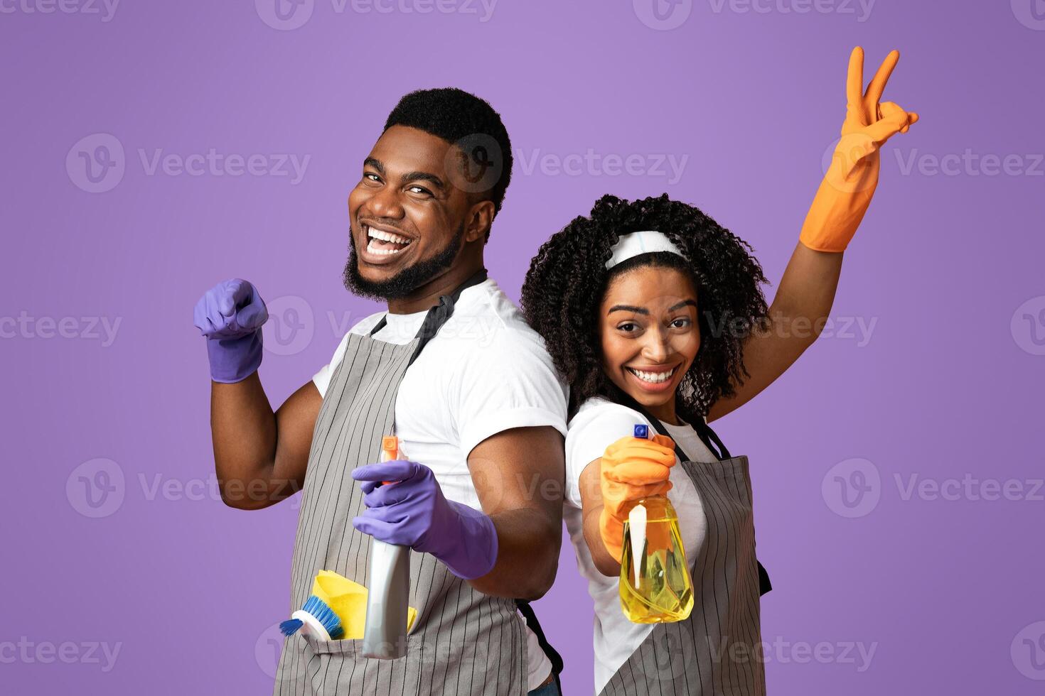 Housekeeping and cleaning service concept. Cheerful african american couple with spray detergents in hands posing over pink background, free space photo