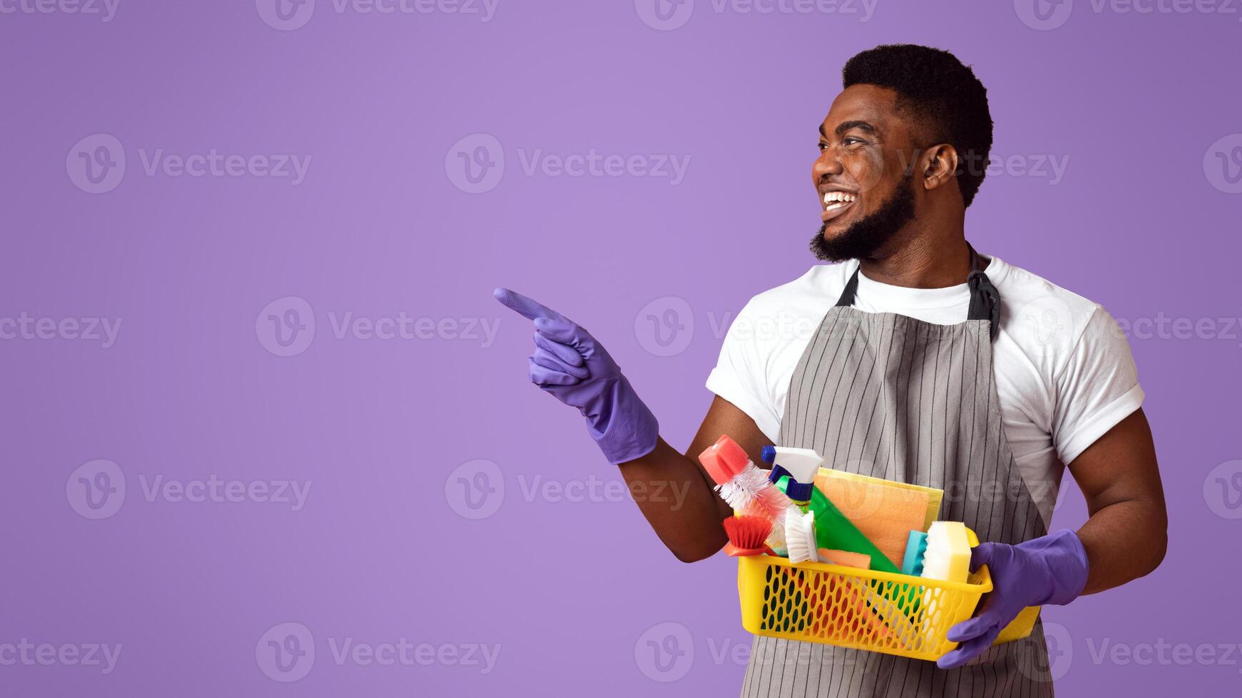 Cleaning Advertisement. Black Male Cleaner With Household Supplies In Hands Pointing Aside At Copy Space On Pink Background, Panorama photo