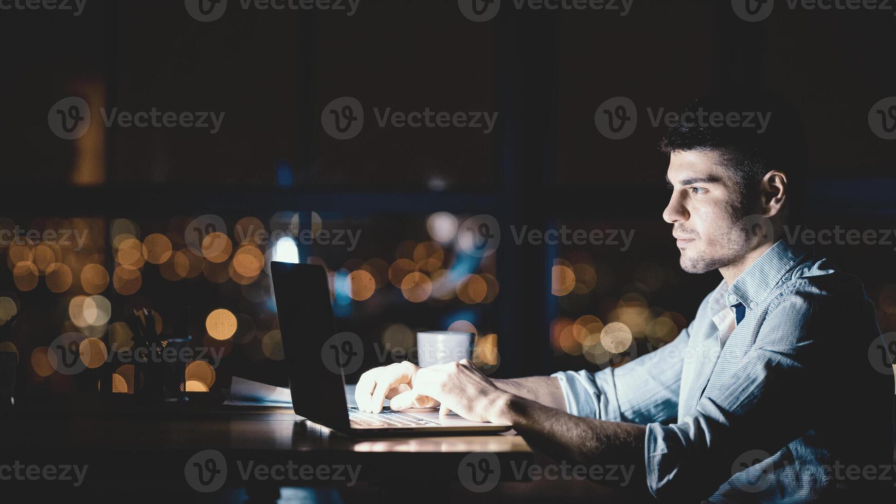 Young Businessman Working On Laptop Overtime Sitting Near Window In Modern Office. Late Night Work. Copy Space, Panorama photo