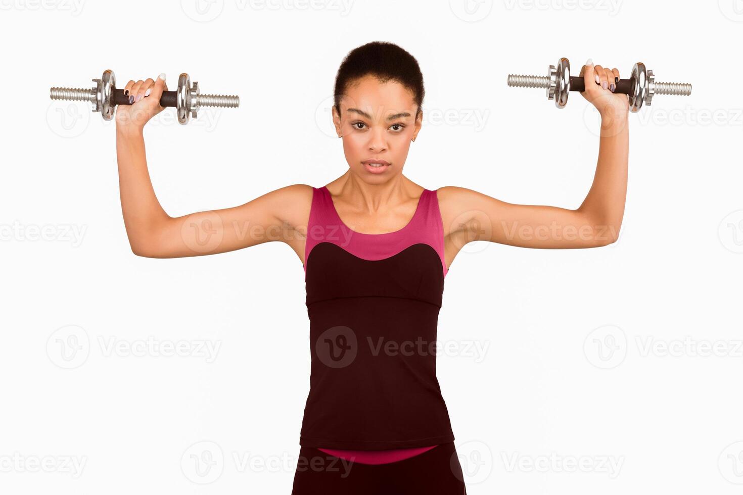 Female Strength Workout. Motivated Afro Girl Holding Dumbbells Exercising Looking At Camera Standing Over White Background. Studio Shot photo