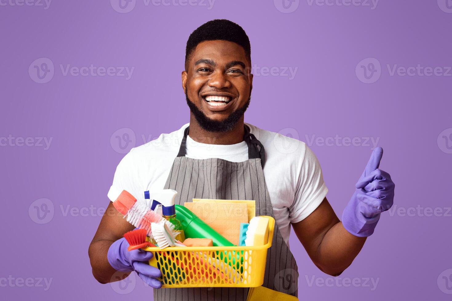 Cleaning With Pleasure. Positive Black Man Holding Container With Detergents And Household Supplies And Showing Thumb Up Over Pink Background photo