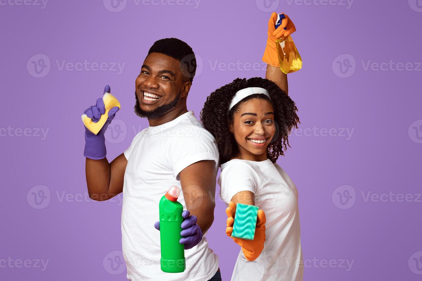 Joyful Spring-Cleaning. Portrait Of Cheerful Black Couple With Sponges And Detergents In Hands Posing On Pink Background In Studio photo