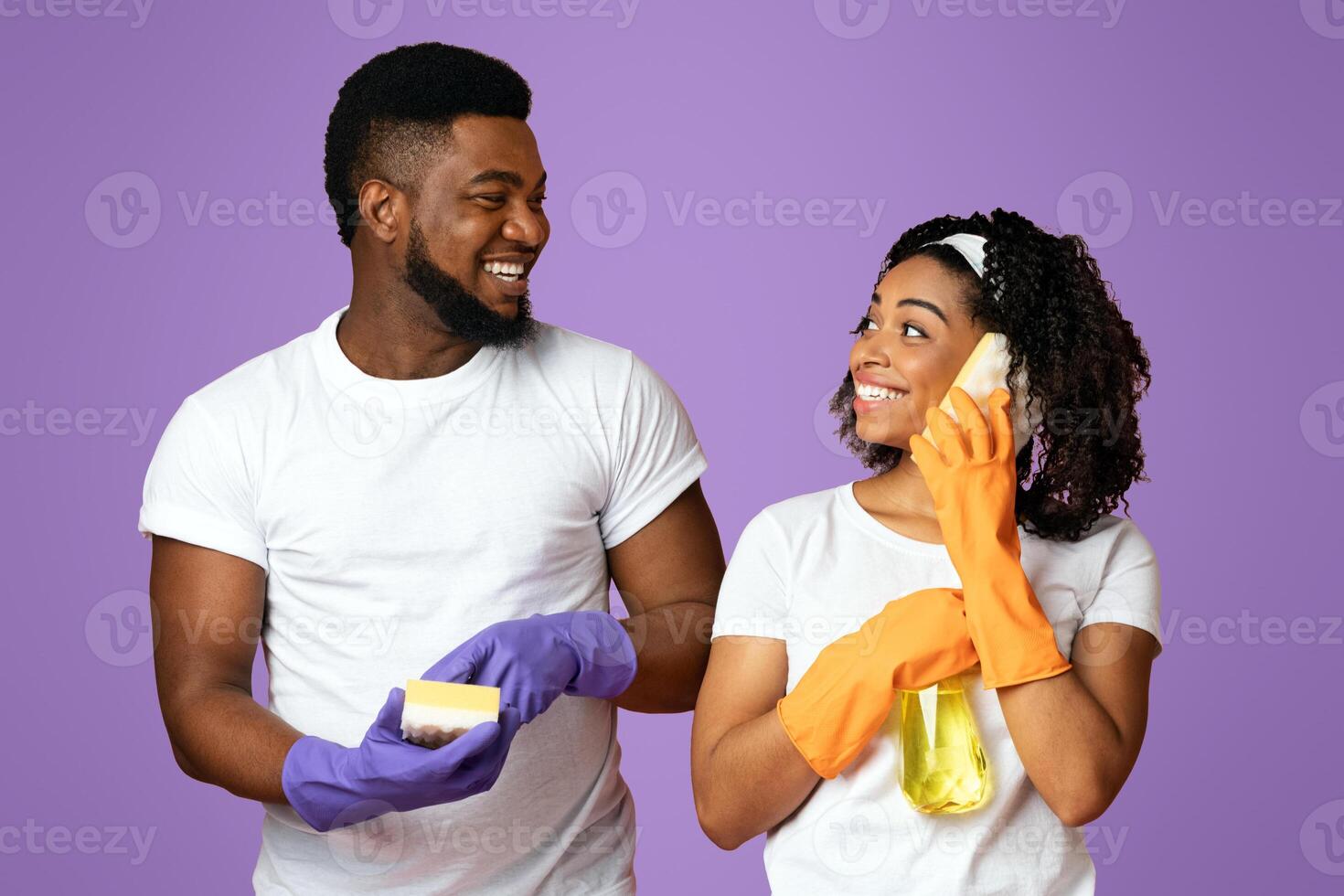 Crazy Cleaning. Joyful young couple using sponges like cellphones, having fun together while tidying home, pink background with free space photo