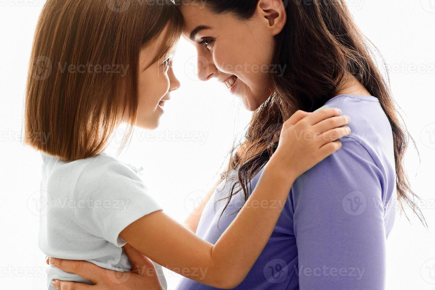 Loving pregnant mother cuddling with little daughter over white background photo