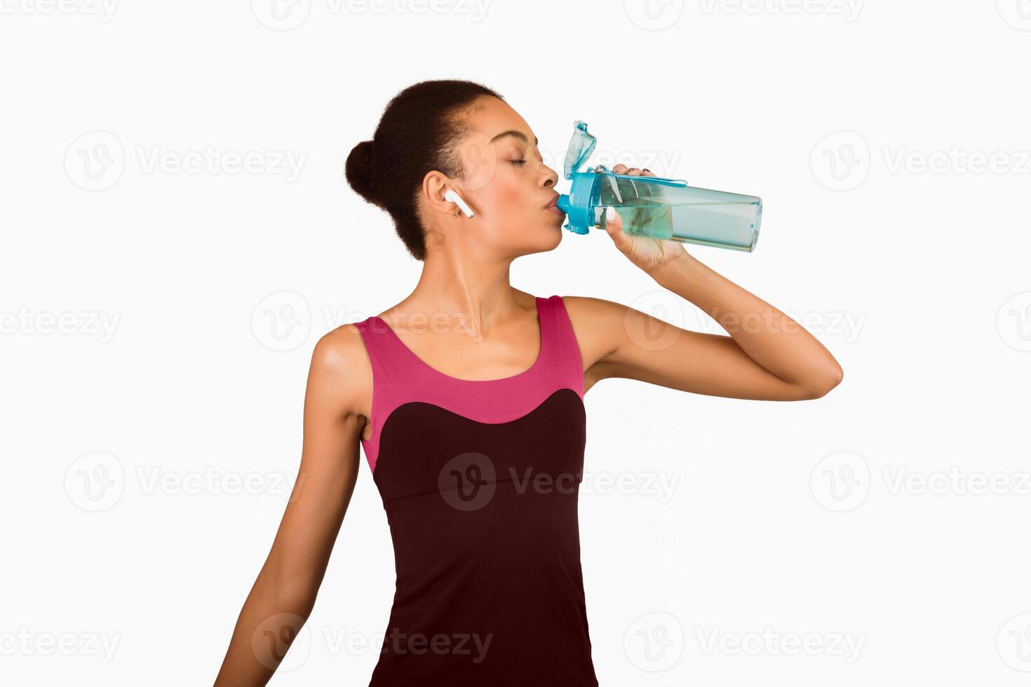 Hydration And Workout. Fit Afro Girl Drinking Water From Bottle Standing Over White Studio Background. Isolated photo