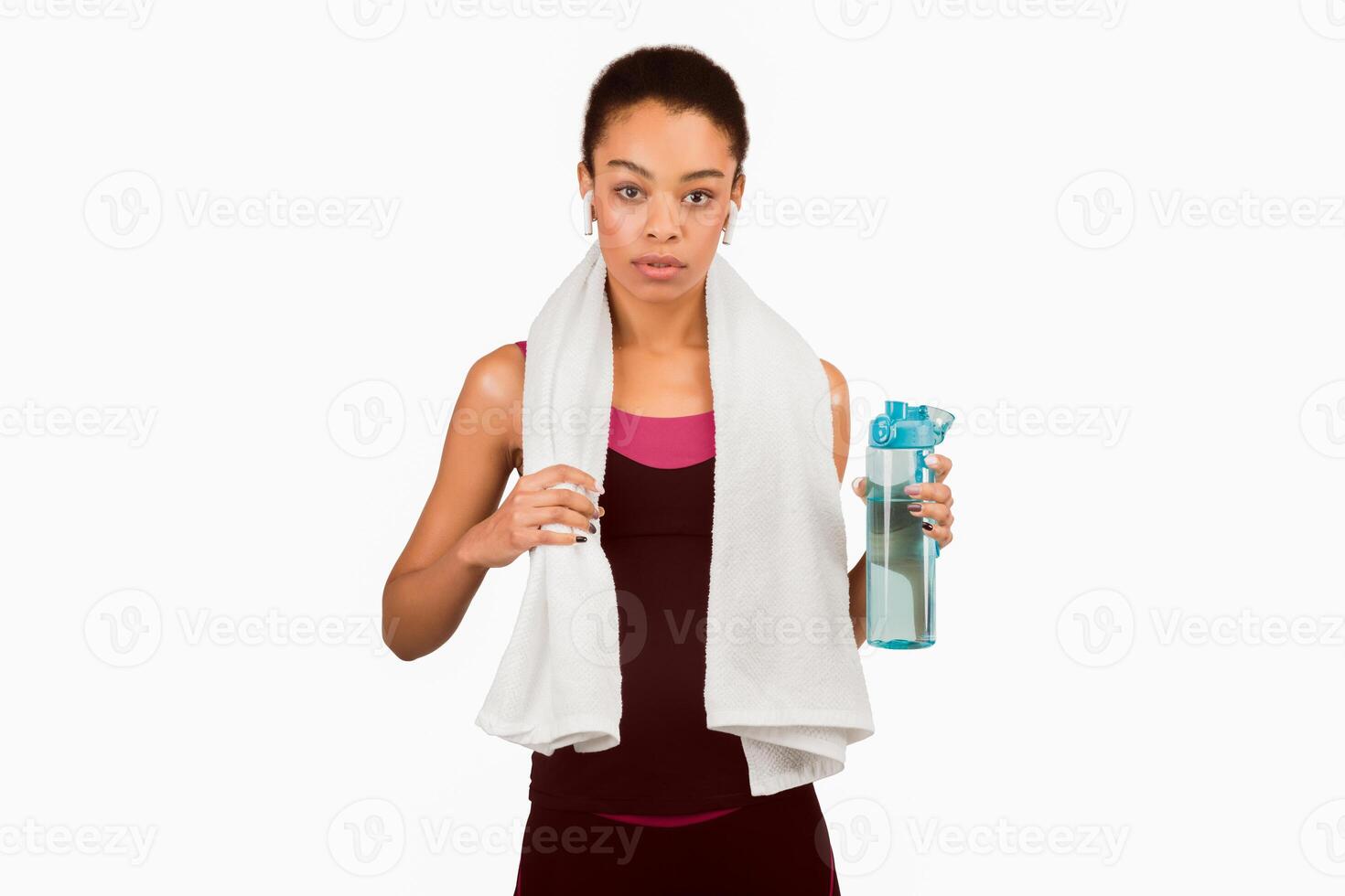 Sporty Lifestyle. Determined African American Girl In Earphones Holding Bottle Of Water Standing Over White Studio Background. Isolated photo
