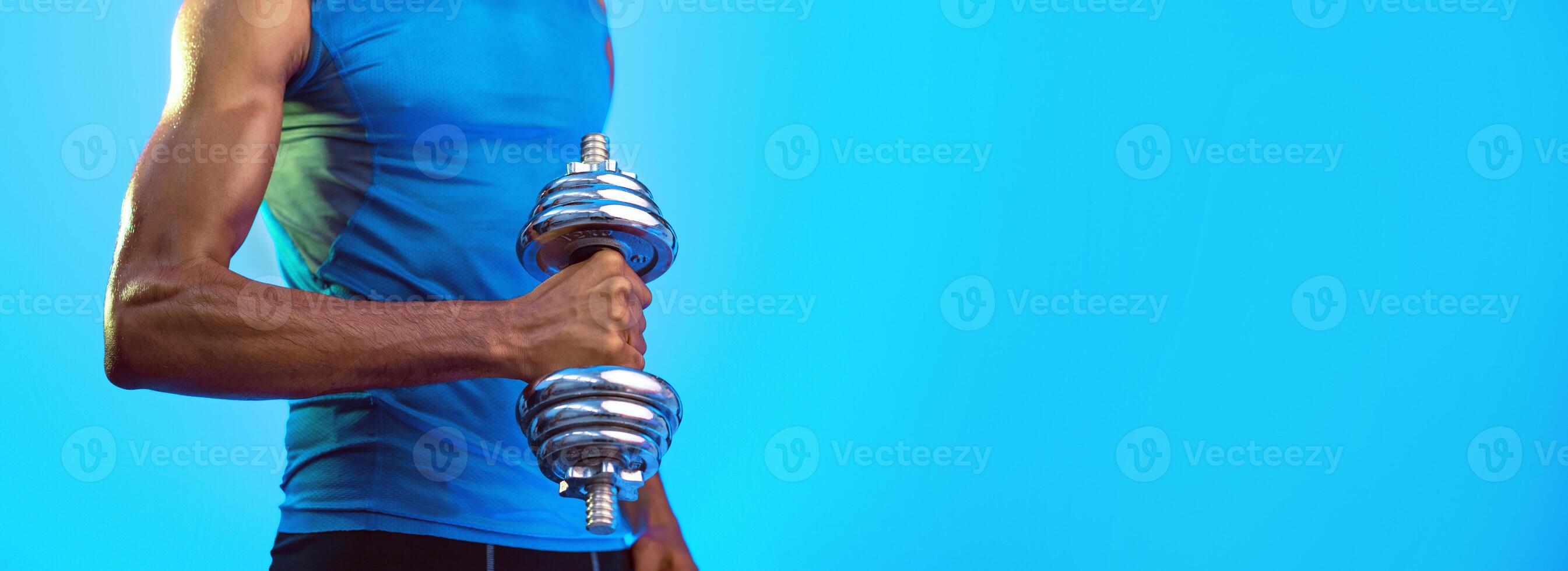 Unrecognizable African American Sporty Guy Exercising With Dumbbell On Blue Background In Studio. Selective Focus, Panorama photo