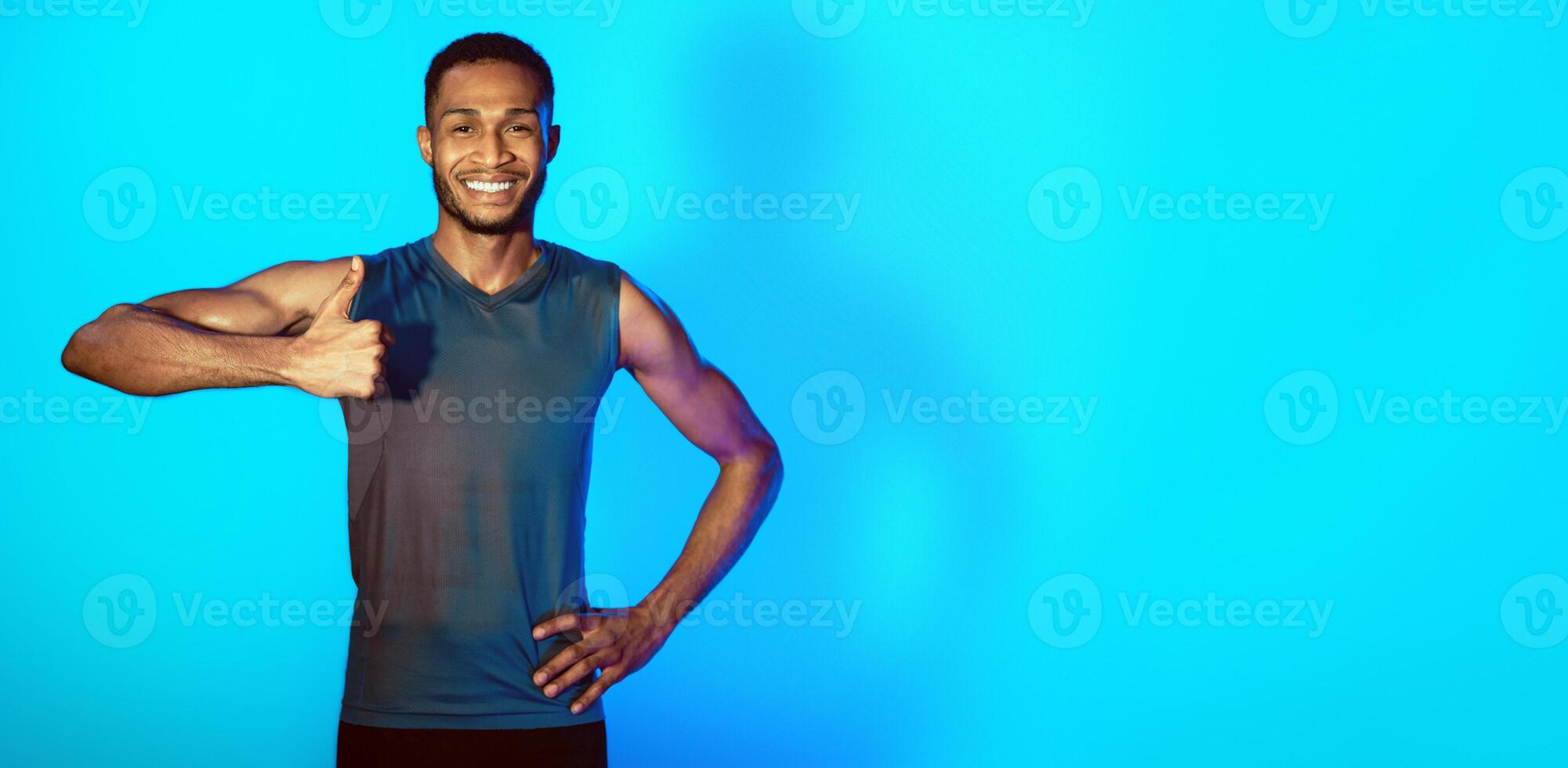 I Like Workout. Fit Man Gesturing Thumbs Up Smiling To Camera Standing Over Blue Studio Background. Copy Space, Neon Lights photo