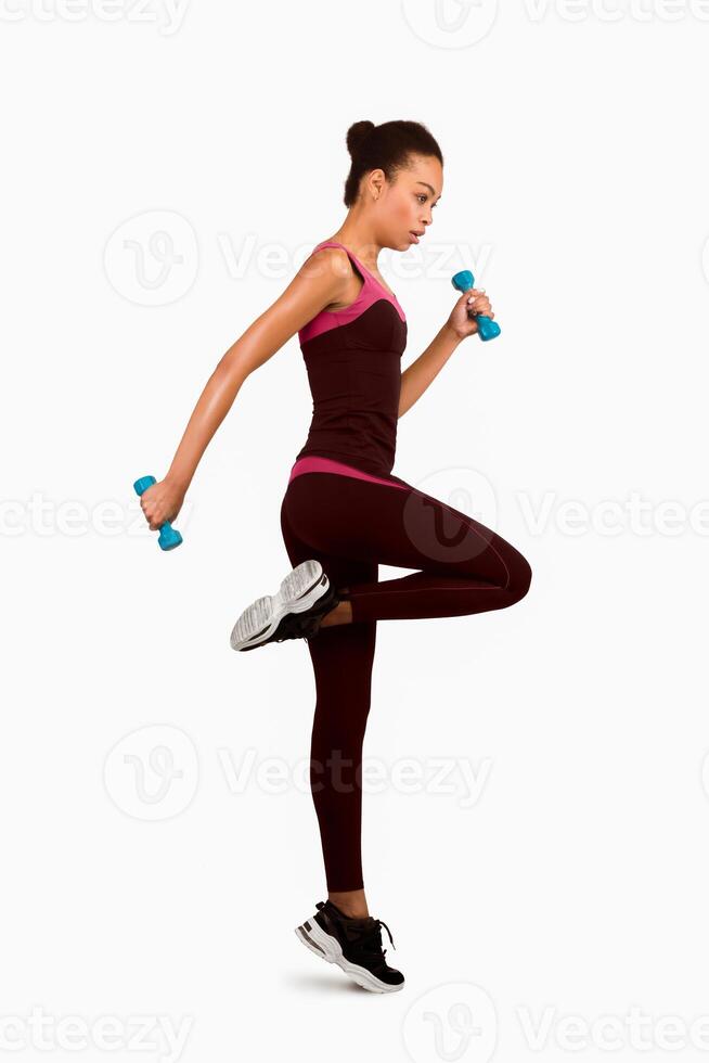 Afro Fitness Lady Exercising Jumping With Dumbbells On White Studio Background. Full Length, Isolated photo